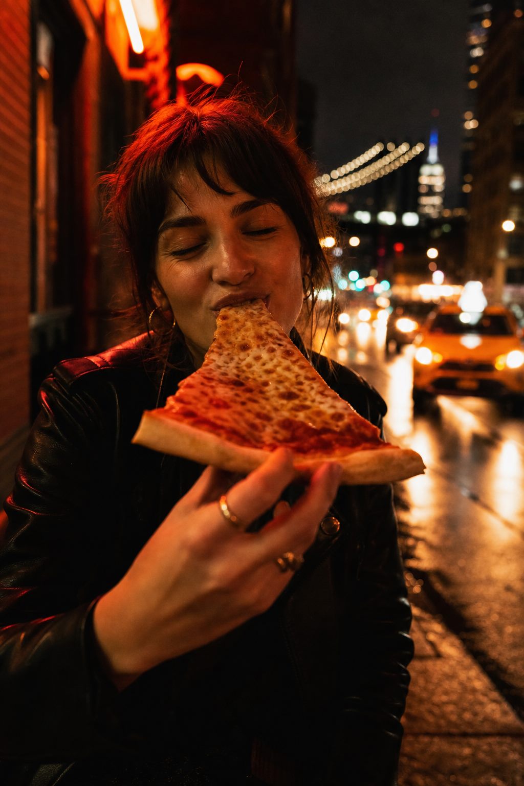 Person eating a folded New York slice on a Brooklyn street at night