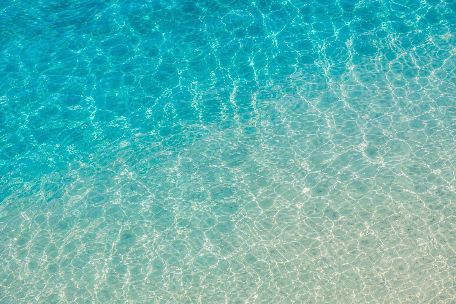 Aerial view of turquoise sunlit water with sand caustics